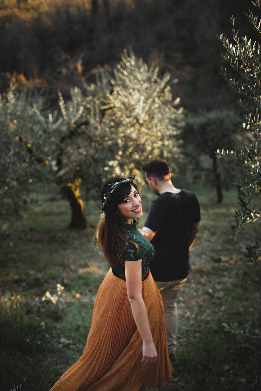 Coppia che cammina mano nella mano in mezzo agli ulivi, ragazza con corona di ulivo e vestito verde e arancione