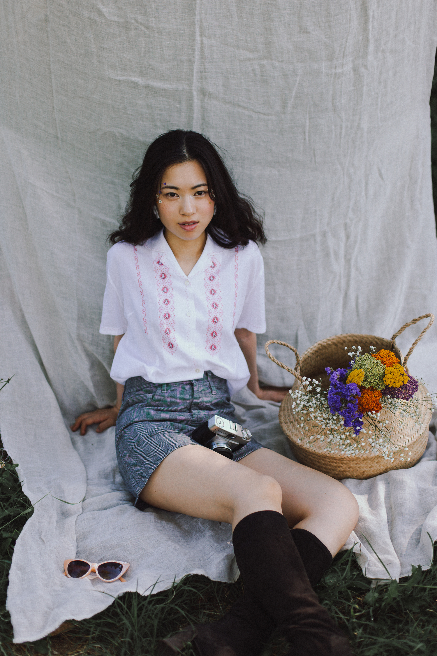 Ritratto di ragazza seduta con macchina fotografica vintage, gonna, camicia e fiori, anni '60